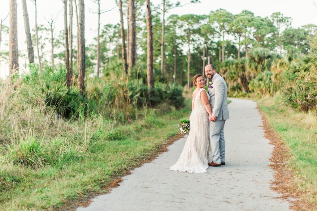 bride and groom walking down path surrounded by green trees