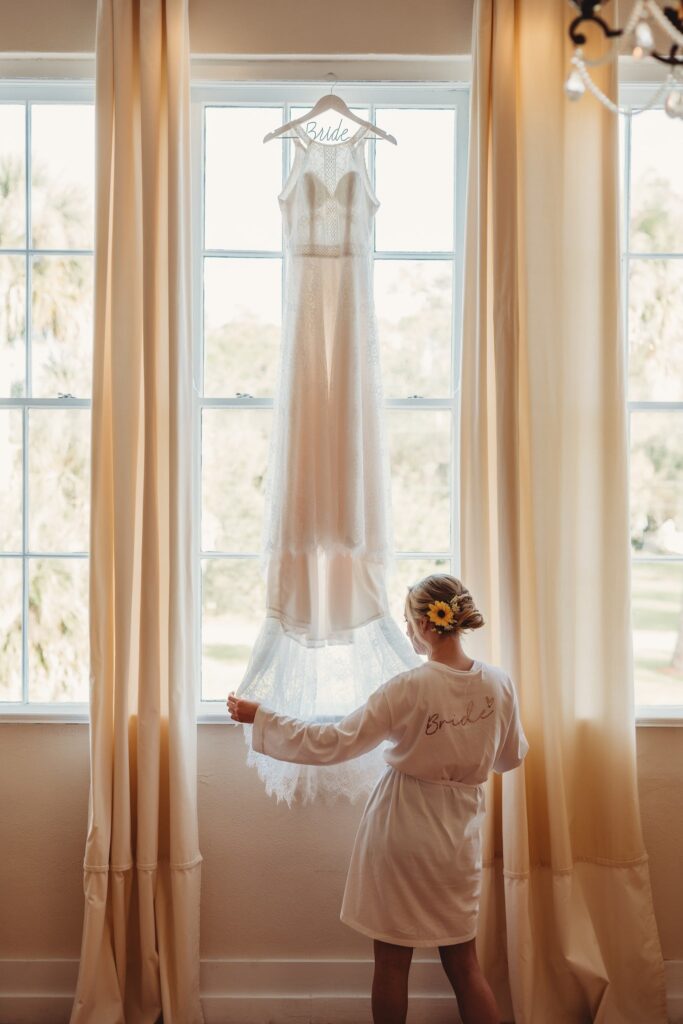 bride looking at her gown hanging in windows