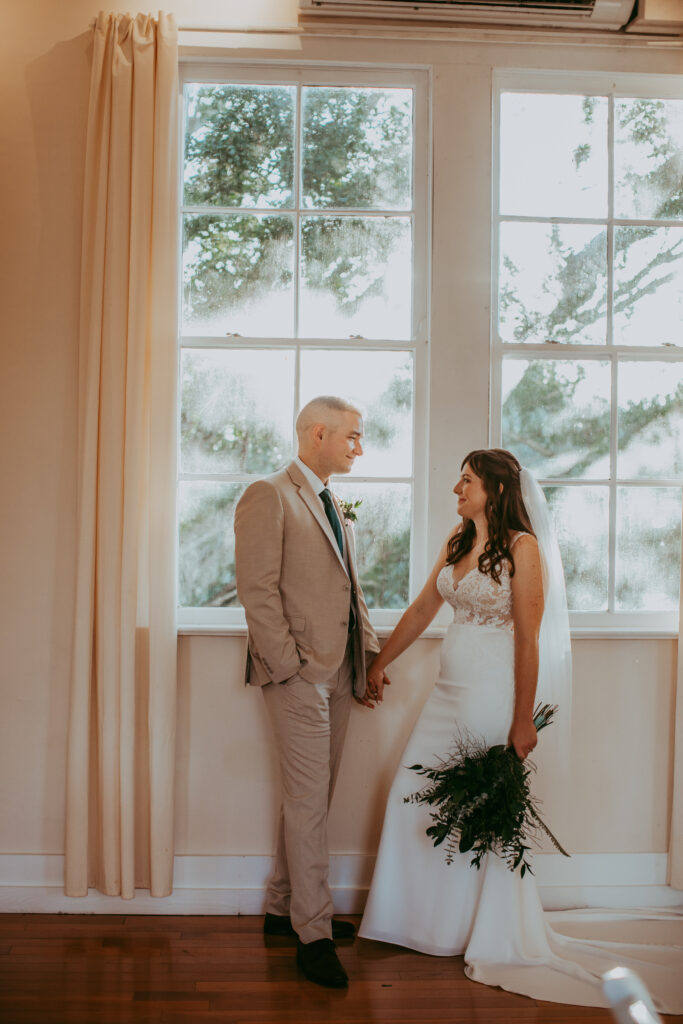 bride and groom holding hands in front of window