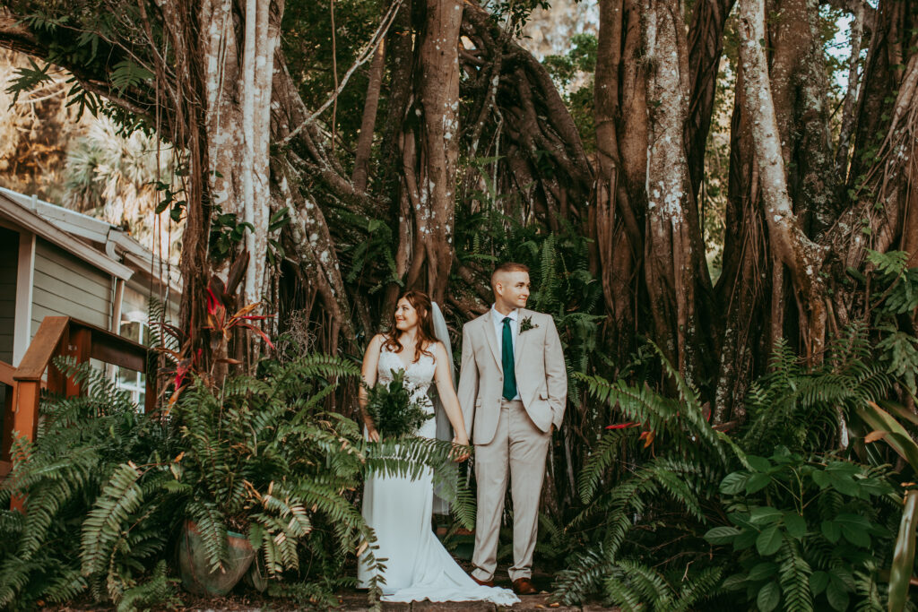 bride and groom standing surrounded by ferns