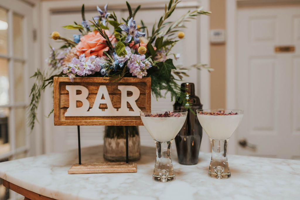 wooden bar sign with flower arrangement at wedding